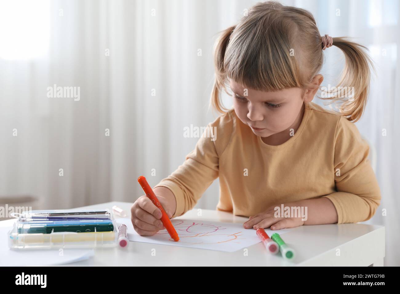 Cute little girl drawing with marker at white table indoors. Child`s art Stock Photo